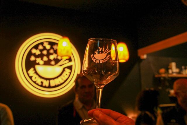 Un verre gravé au logo Wok'n Breizh levé devant l'enseigne lumineuse du restaurant